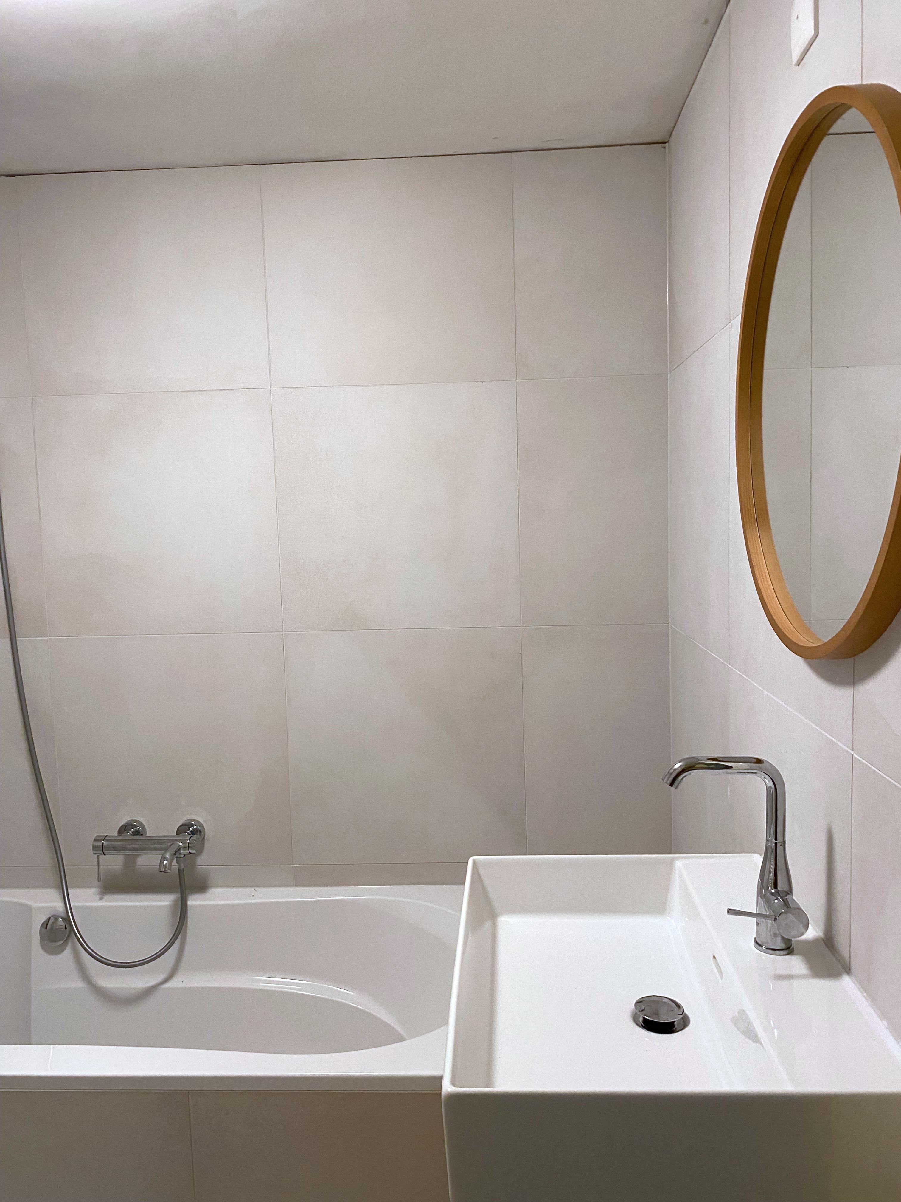 Gerenoveerde badkamer met ligbad, wastafel op eikenhouten meubel, ronde spiegel en grootformaat wandtegels — uitgevoerd door Smillywood in Noord-Nederland