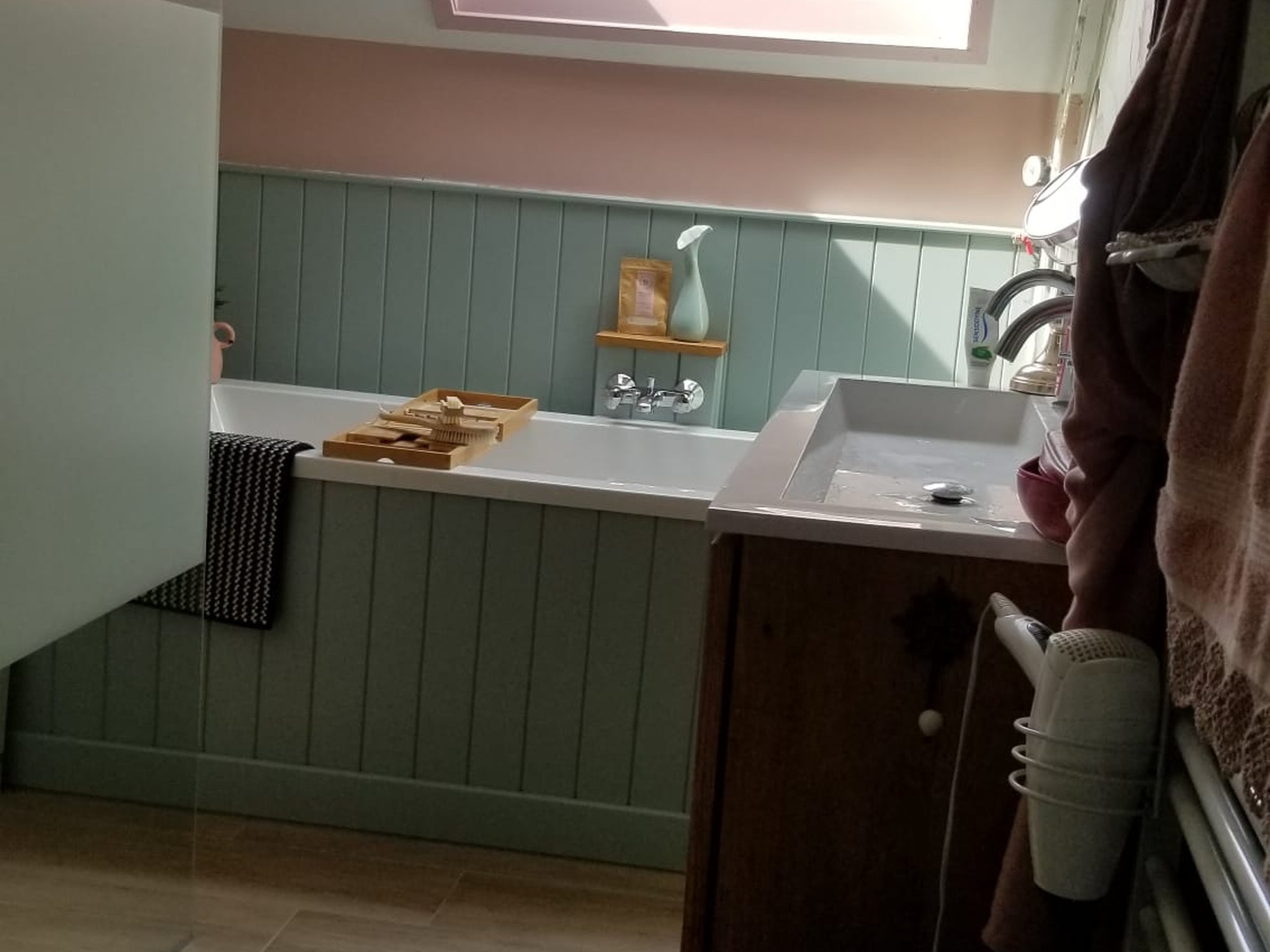 Overzicht van de gerenoveerde badkamer in Britse stijl met ligbad, eucalyptusgroene lambrisering, dakraam en wastafel