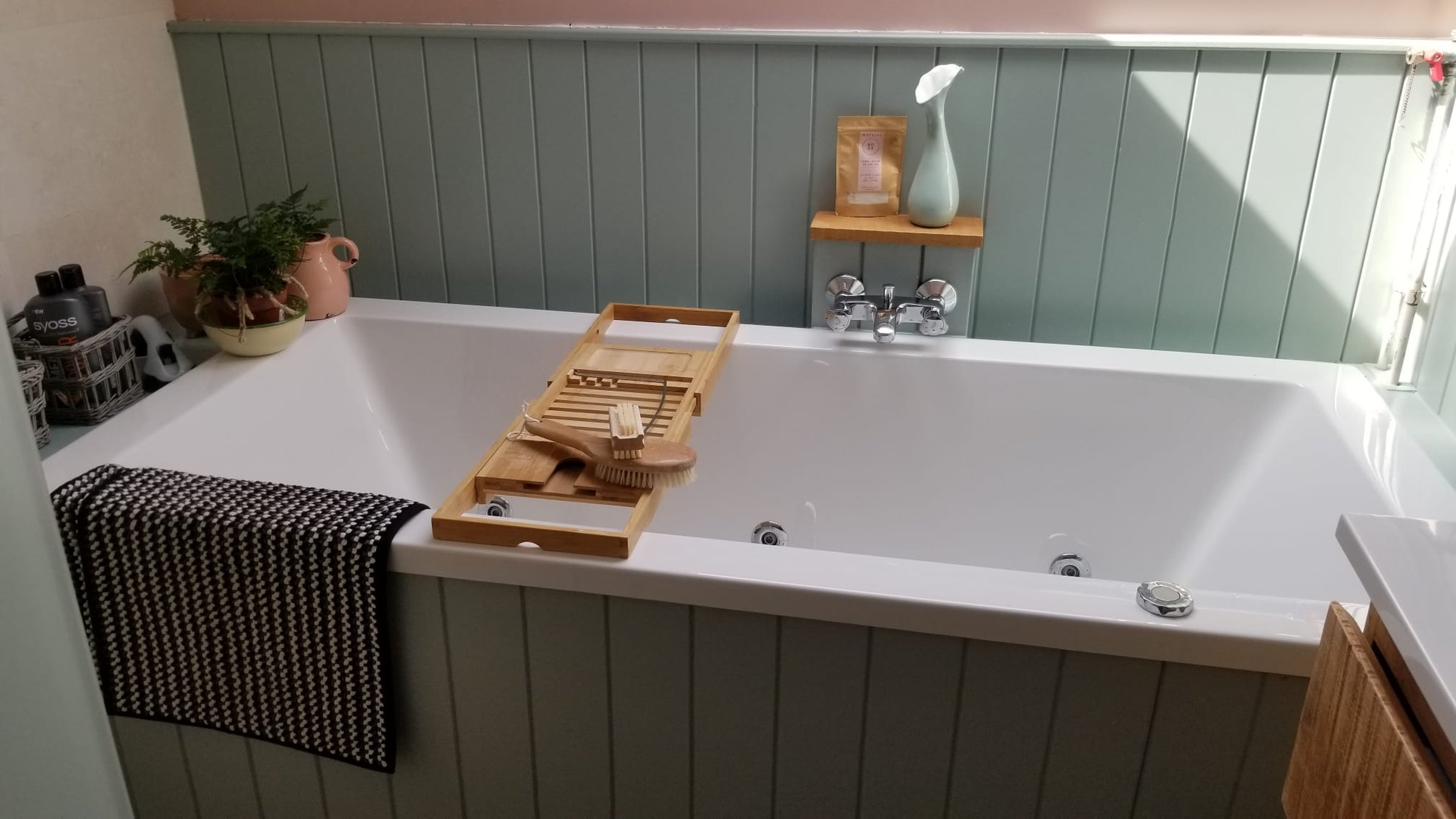 Gerenoveerde badkamer in Britse stijl in Hoogezand met wit ligbad, eucalyptusgroene lambrisering en houten badplank onder een schuin dak