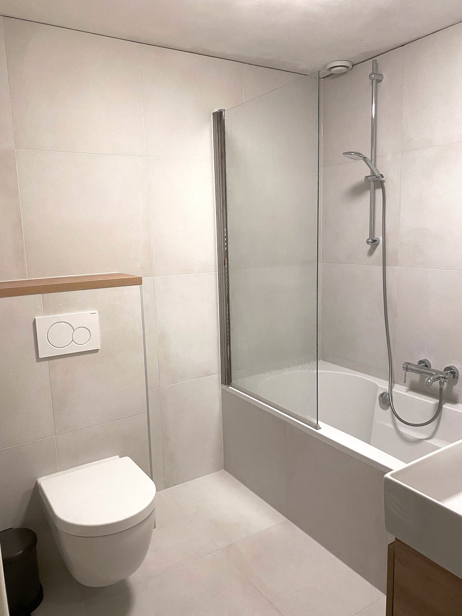 Overzicht van de gerenoveerde badkamer in Assen Marsdijk met ligbad, douchewand, wandhangend toilet en lichte tegels